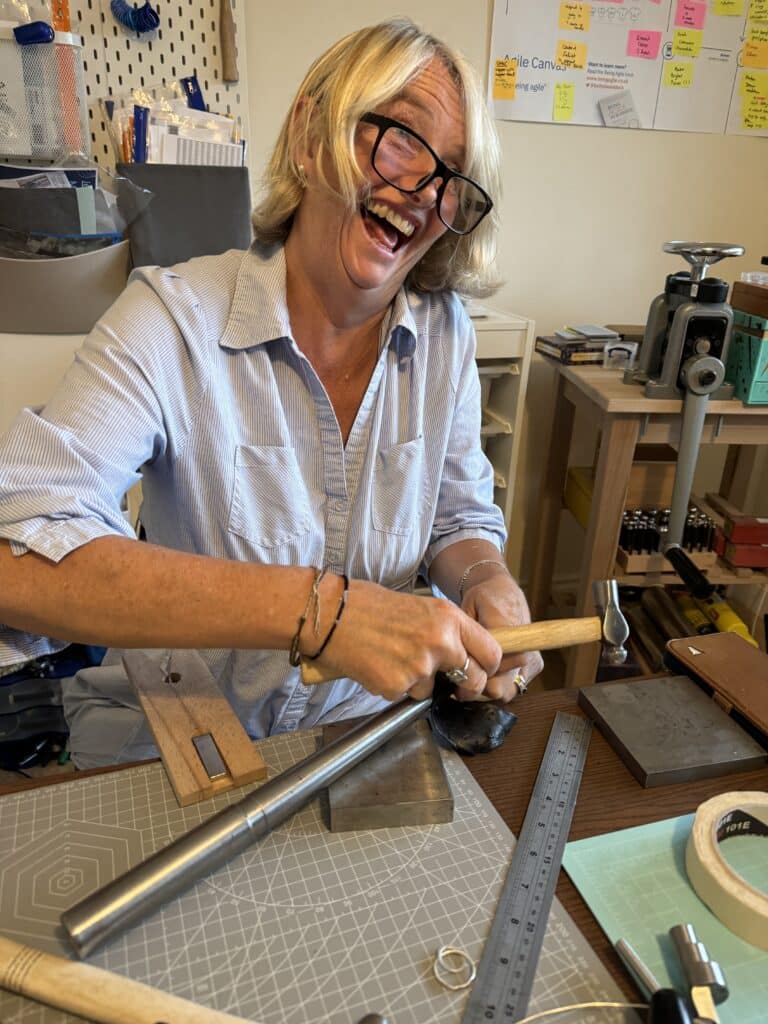 A student smiling while crafting silver earrings during a jewellery-making course in Cornwall, guided by me in a hands-on workshop setting.