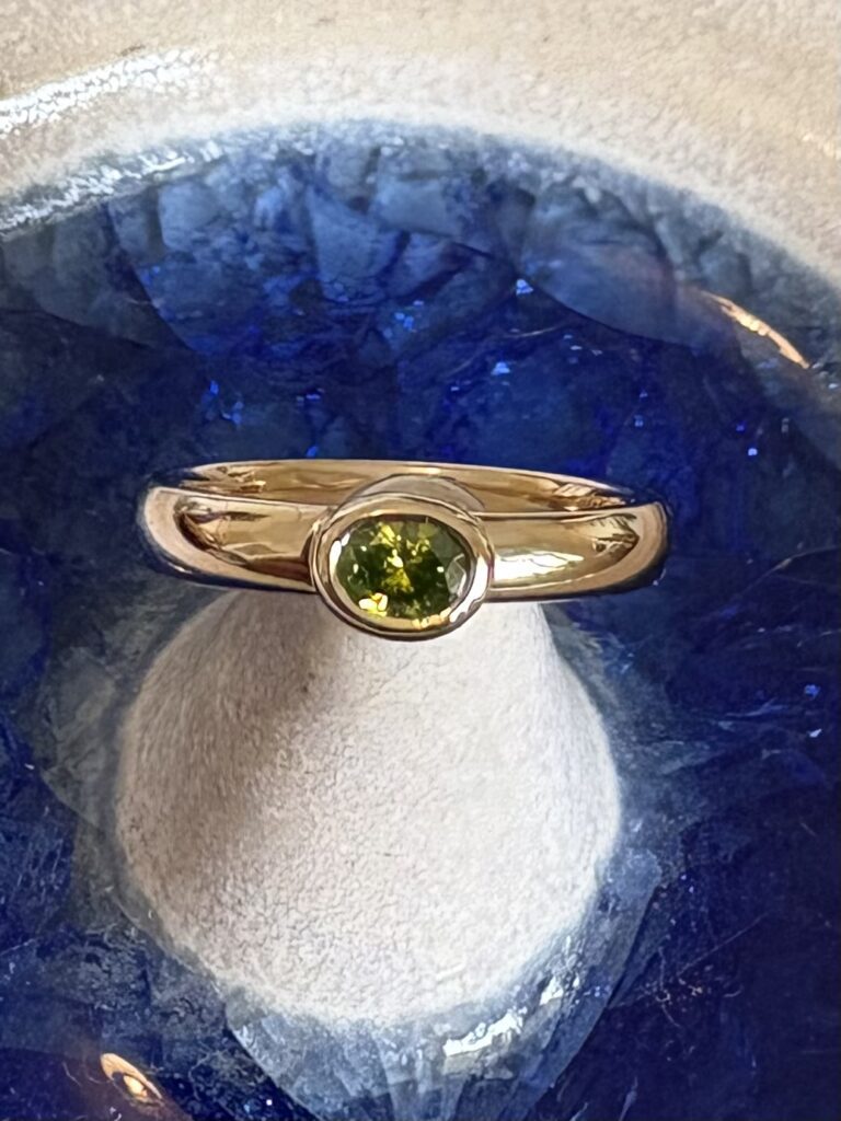 Gold engagement ring with an oval green diamond displayed on blue glass.