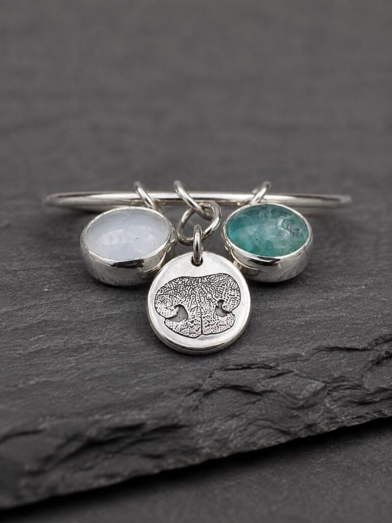 birthstone-and-nose-print-memorial-bangle-detail Silver memorial bangle with birthstone charms and a pet nose-print charm created from a photograph.