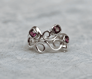 Organic silver wave ring with deep pink ruby-coloured stones on a softly styled neutral background, handmade by Cornovii Silver.